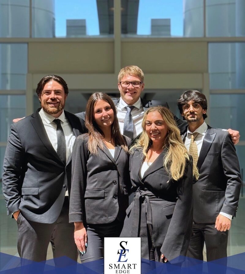 Smart Edge Inc. team members gathered beneath a glass atrium with the downtown skyline behind them
